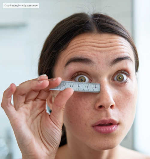 Woman using a ruler to measure her eye shape, demonstrating how to determine eye type for optimal makeup application.